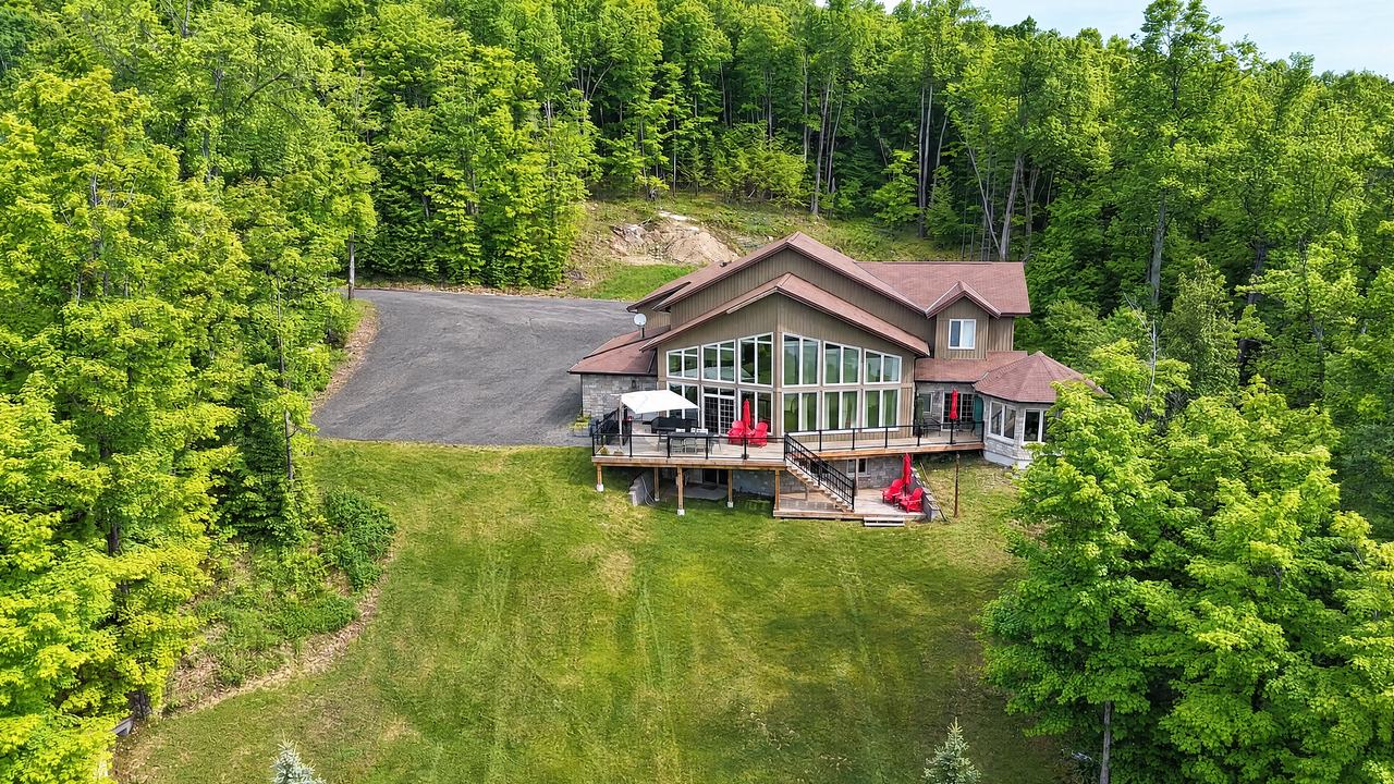 Clubhouse from the air: the house and its lakeside decks at the top of a long lawn, with woods all around