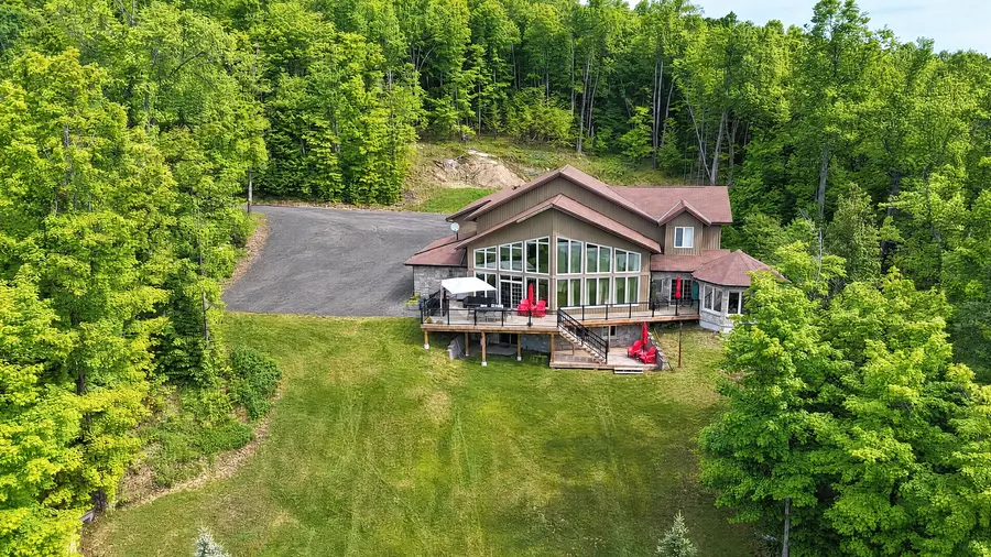 Clubhouse from the air: the house and its lakeside decks at the top of a long lawn, with woods all around
