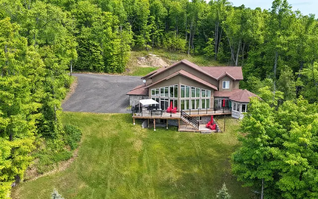 Clubhouse from the air: the house and its lakeside decks at the top of a long lawn, with woods all around