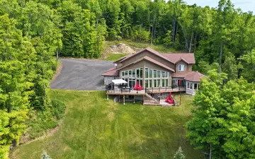Clubhouse from the air: the house and its lakeside decks at the top of a long lawn, with woods all around