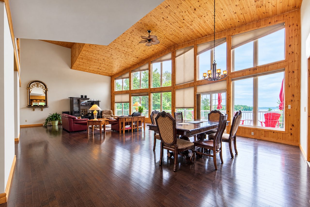 Clubhouse: the great room dining table under a pine ceiling, with tall windows onto the lake
