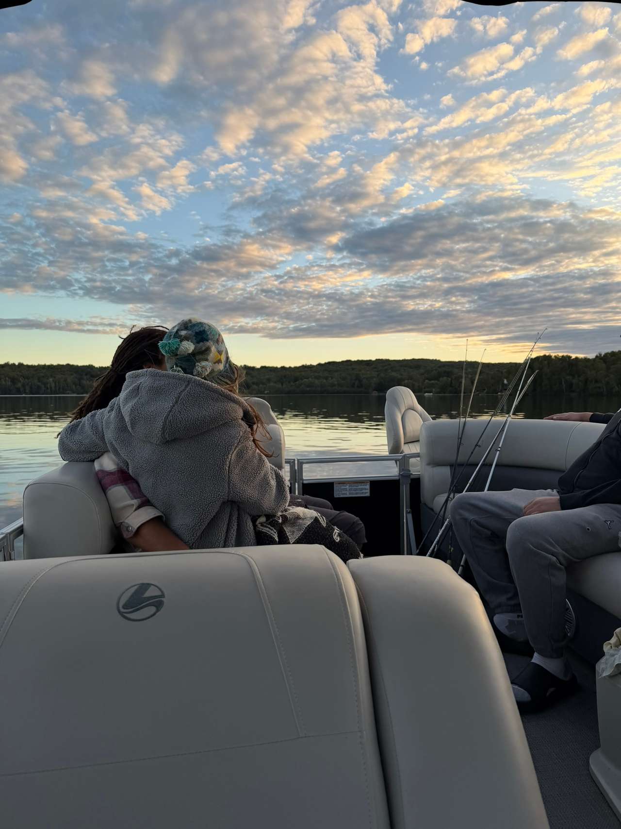 Two people hugging on a pontoon boat beneath a cloud-filled evening sky