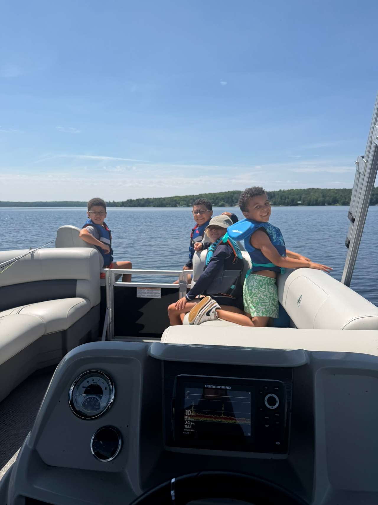 Four children wearing life jackets on a pontoon boat on the lake
