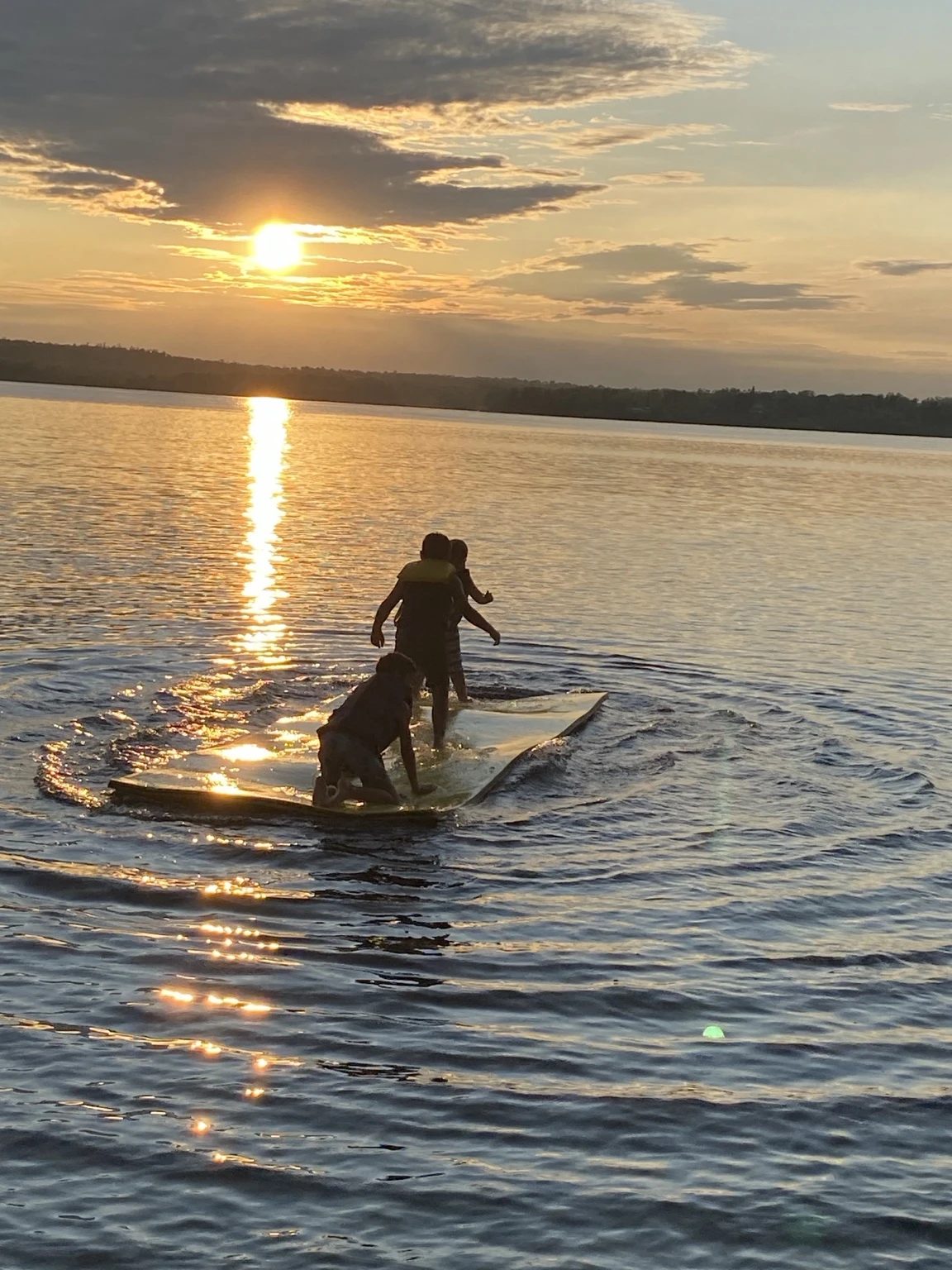 Children playing on a floating mat at sunset on Lake Nosbonsing.