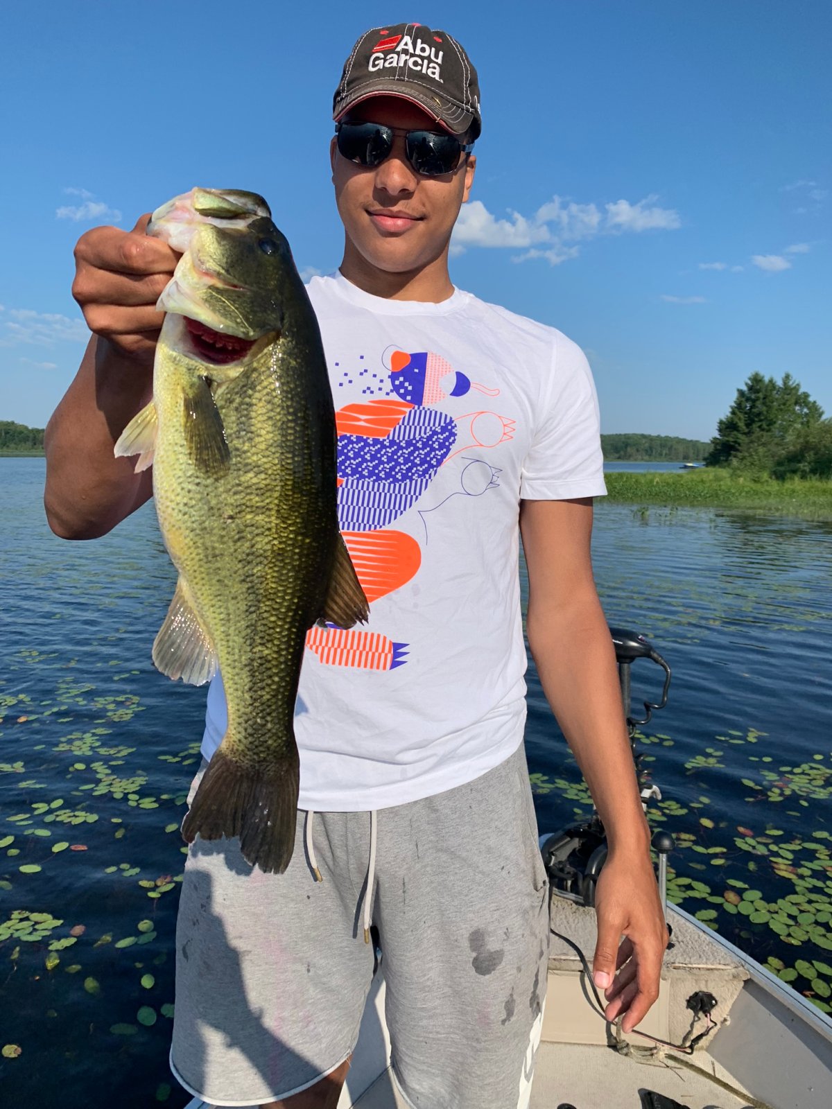 An angler in a cap holding a fish beside lily-covered water