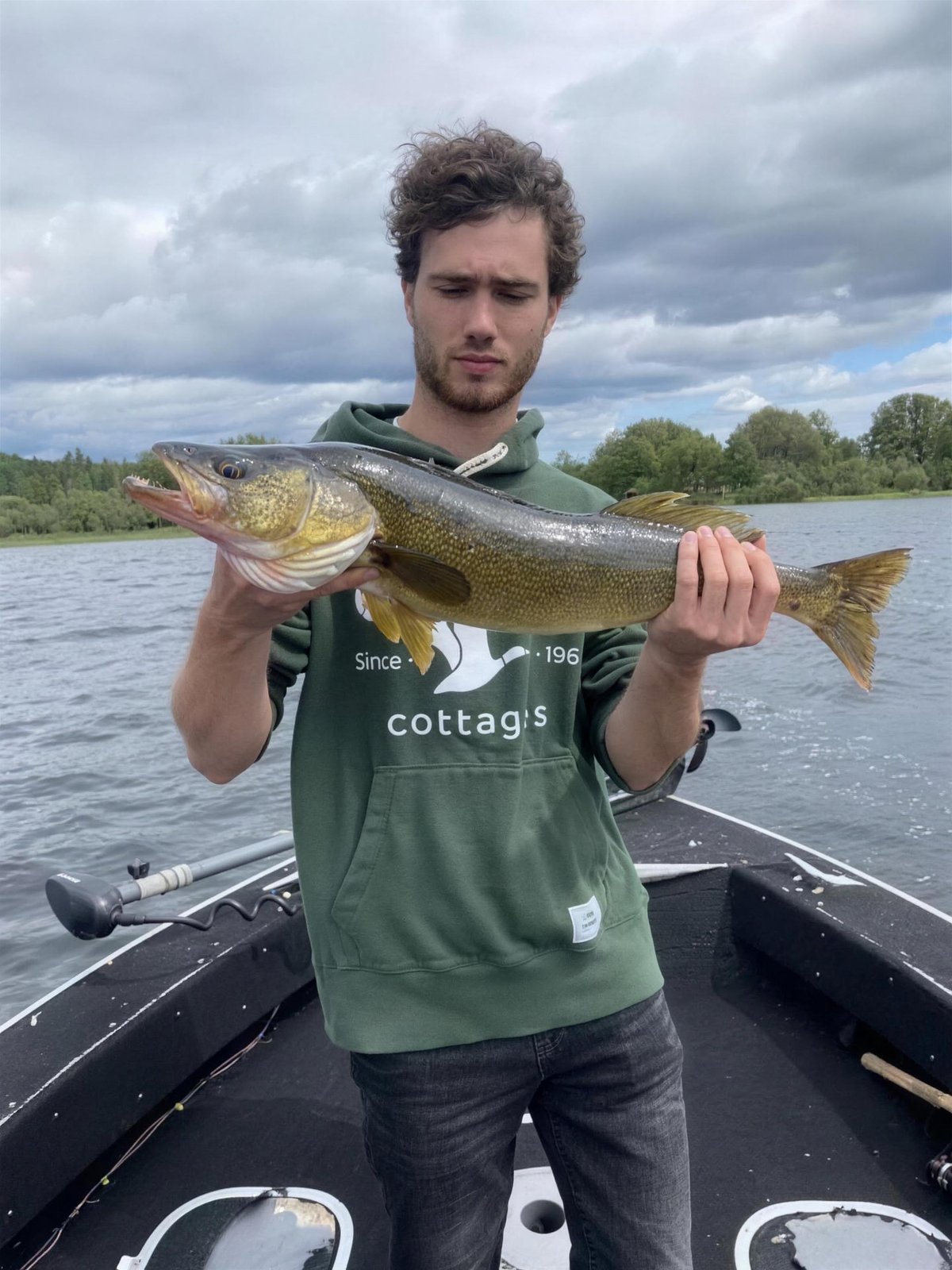 An angler holding a fish across his hands beneath a cloudy sky