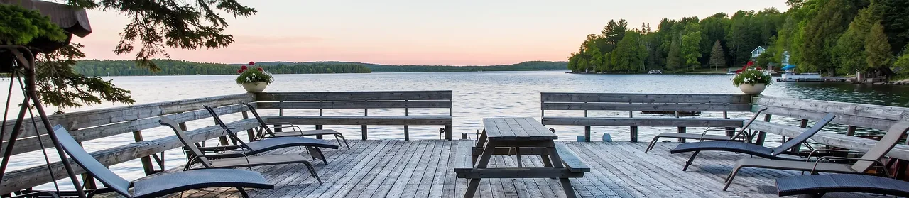 The lakefront sun deck at dusk: a picnic table between benches along the railing, and Lake Nosbonsing under a pink sky