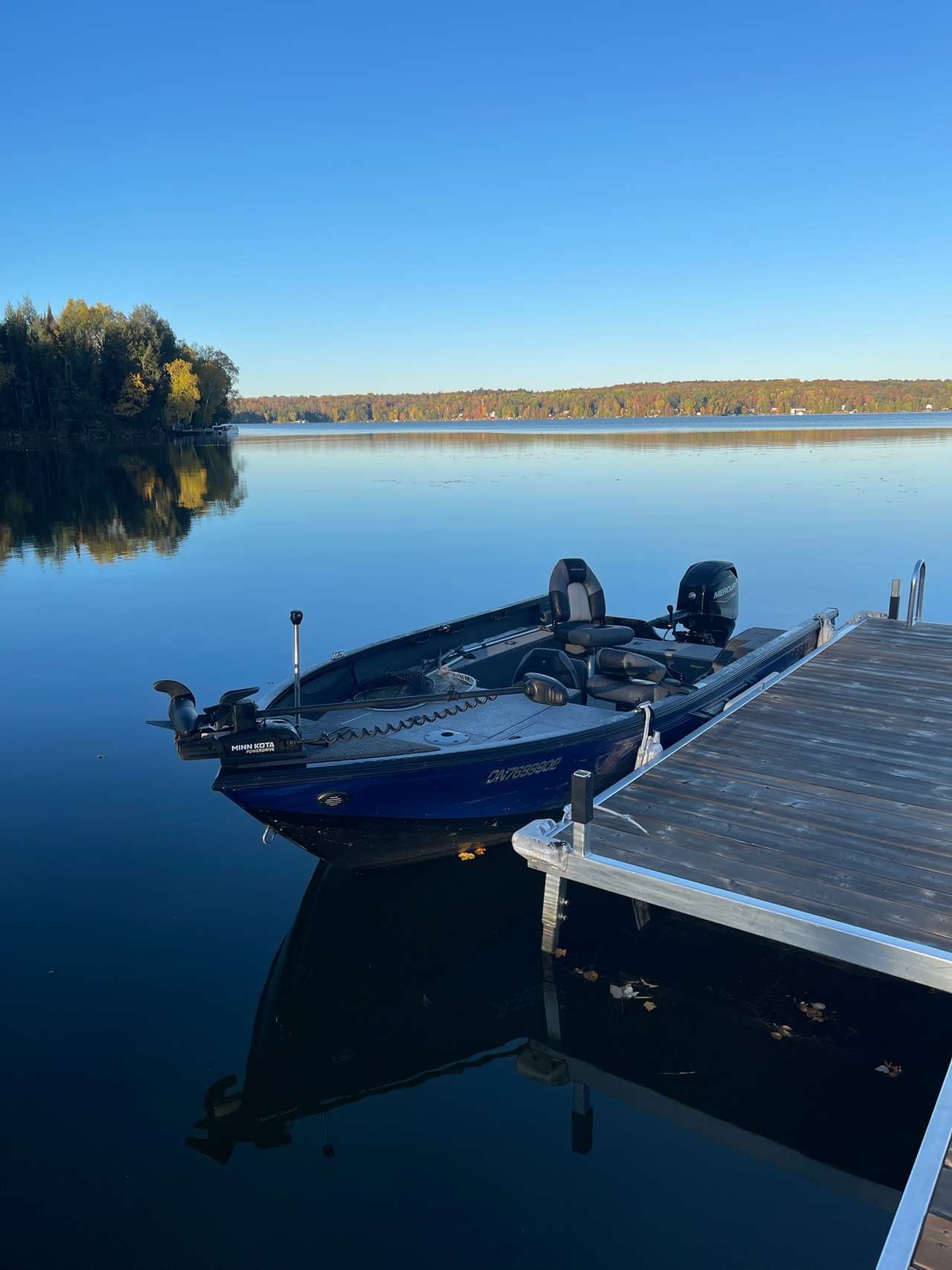 The blue Crestliner fishing boat beside the dock on a calm autumn morning