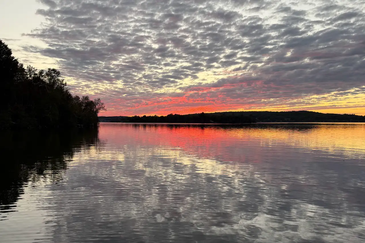 Sunset over Lake Nosbonsing: the sky glowing pink and orange above the wooded far shore, mirrored in the calm water