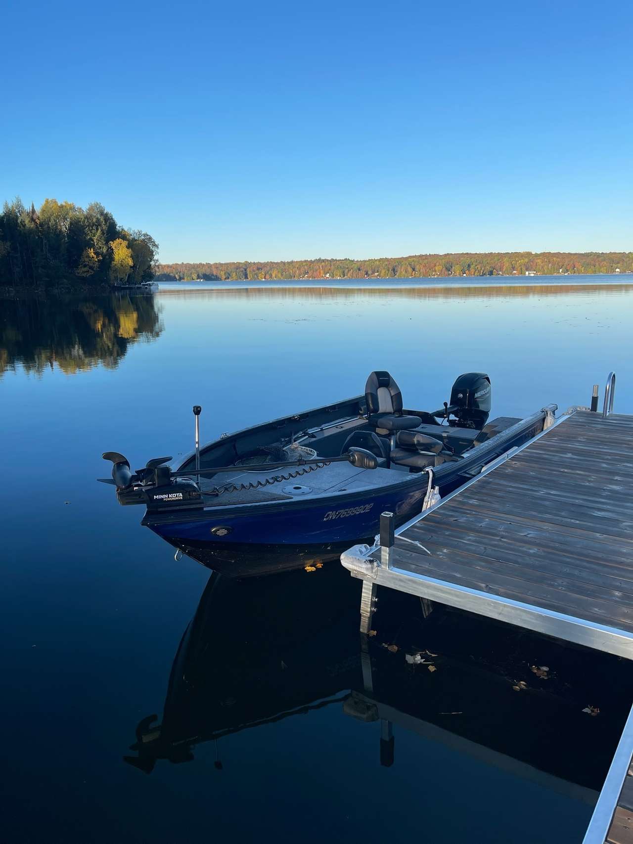 A blue fishing boat moored beside the dock on calm Lake Nosbonsing