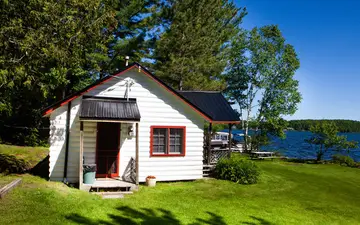 Loon Landing, a white cottage with red trim, with the lake behind it