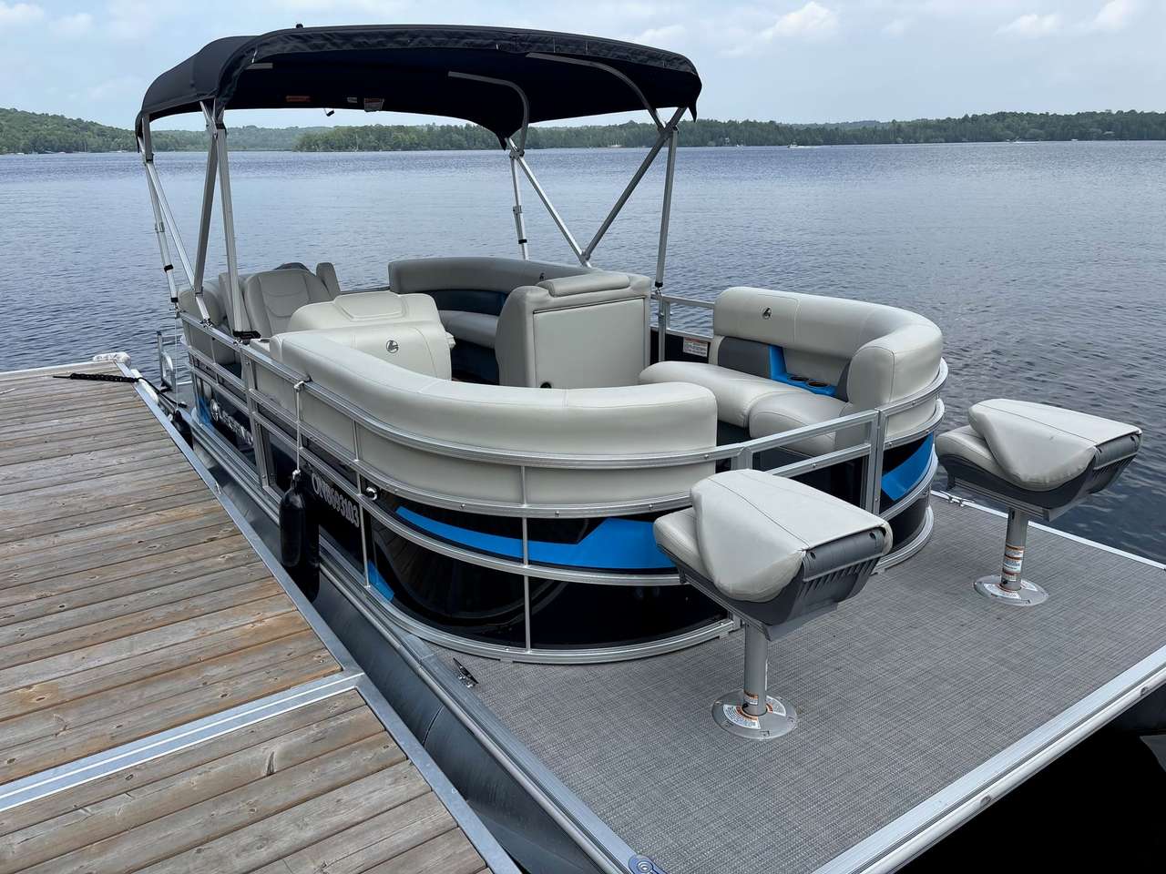 The 18 ft Legend pontoon at the dock, seen from the front, with blue trim and two fishing seats on its front deck