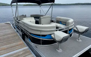 The 18 ft Legend pontoon at the dock, seen from the front, with blue trim and two fishing seats on its front deck