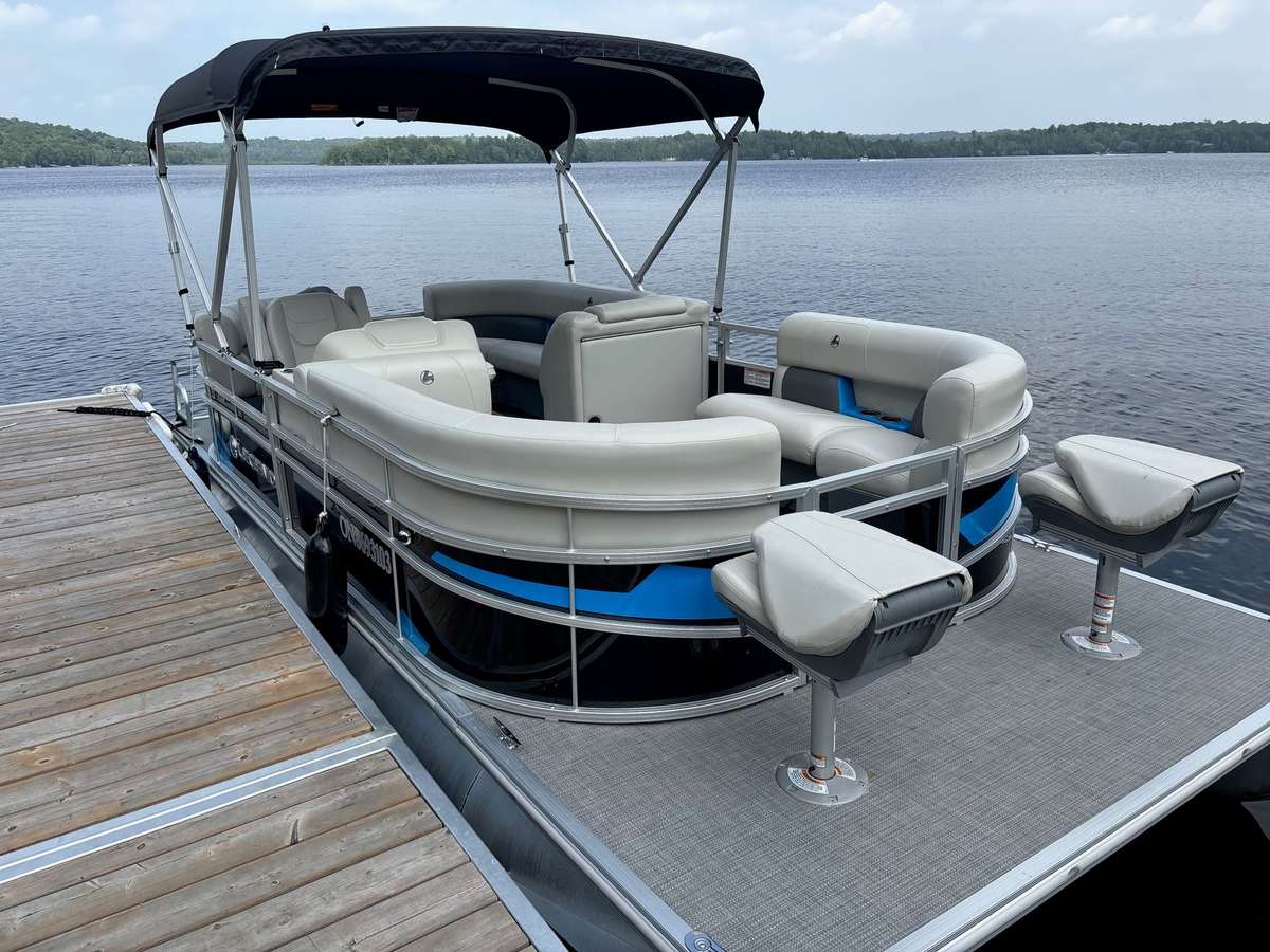The 18 ft Legend pontoon at the dock, seen from the front, with blue trim and two fishing seats on its front deck