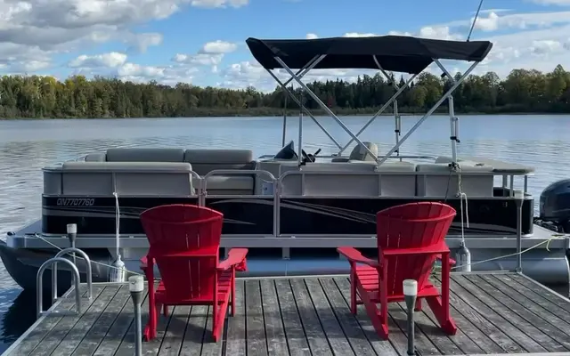 The 20 ft Legend pontoon with its canopy up, moored behind two red chairs on the dock