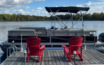 The 20 ft Legend pontoon with its canopy up, moored behind two red chairs on the dock