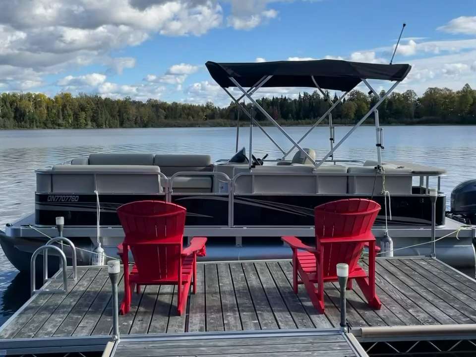 The 20 ft Legend pontoon with its canopy up, moored behind two red chairs on the dock