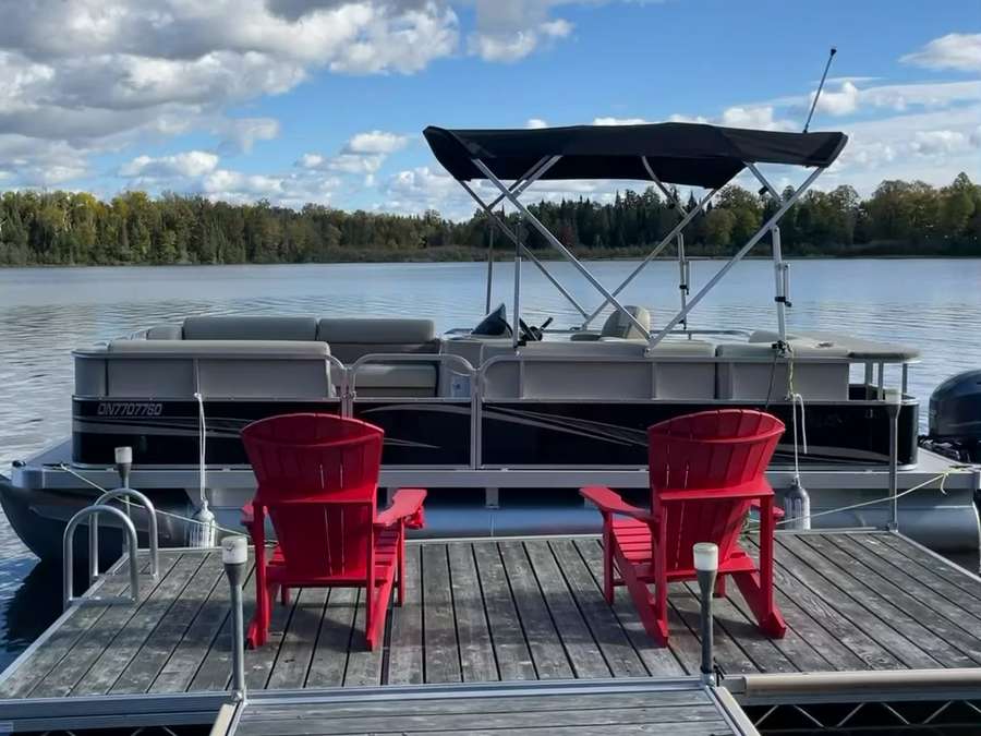 The 20 ft Legend pontoon with its canopy up, moored behind two red chairs on the dock