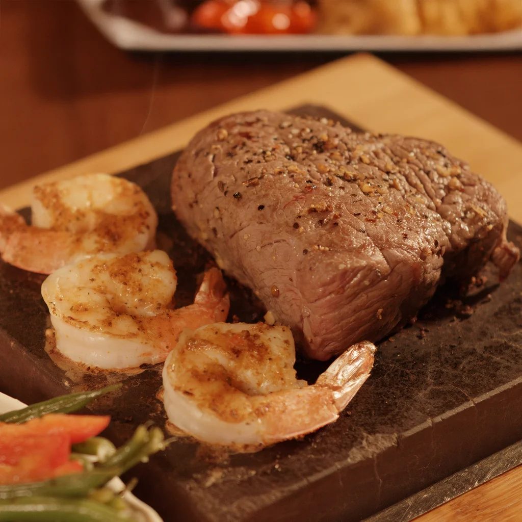Steak and grilled shrimp served on a hot stone with vegetables