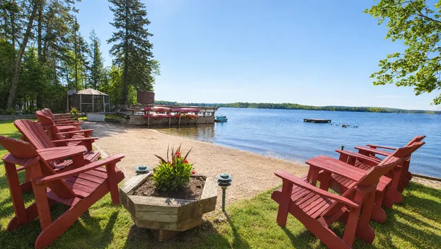 Red wooden Adirondack chairs around the sandy beach, with open access to Lake Nosbonsing and the shoreline beyond