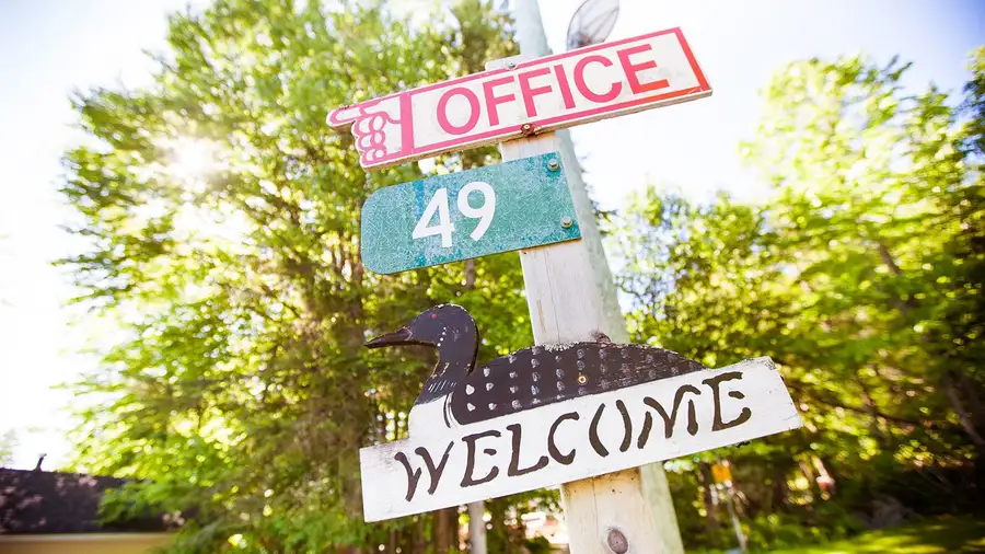 The camp signpost pointing to the office at number 49, with a carved loon and a Welcome sign