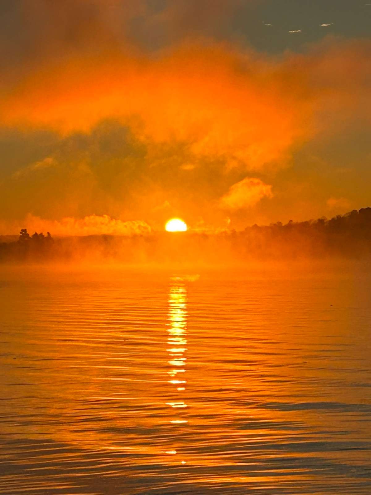 The sun rising through orange mist over the lake, its light a bright path across the rippled water